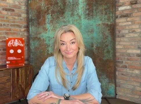Martyna Wojciechowska podczas wyprawy, z uśmiechem i w tle górskim krajobrazem, symbolizująca jej ducha podróży i determinację.