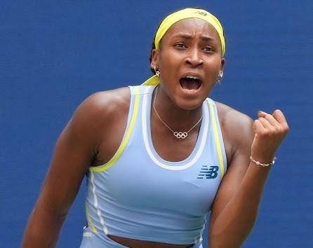 Uśmiechnięta Coco Gauff spoglądająca wprost w obiektyw, w swobodnej pozie, być może z rakietą tenisową, emanująca pozytywną energią.