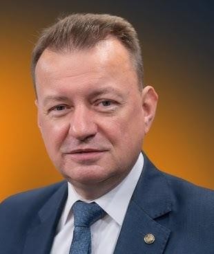 Mariusz Błaszczak jako Minister Obrony Narodowej, w garniturze na tle nawiązującym do wojska.