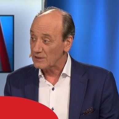 Dariusz Szpakowski w charakterystycznej pozie komentatora, z mikrofonem, dynamicznie gestykulujący, co oddaje jego pasję do sportu.
