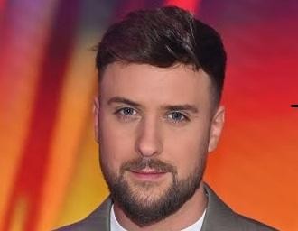 Aleksander Sikora, prezenter telewizyjny, w dynamicznej pozie na planie programu, uśmiechnięty i zaangażowany w interakcję z kamerą.