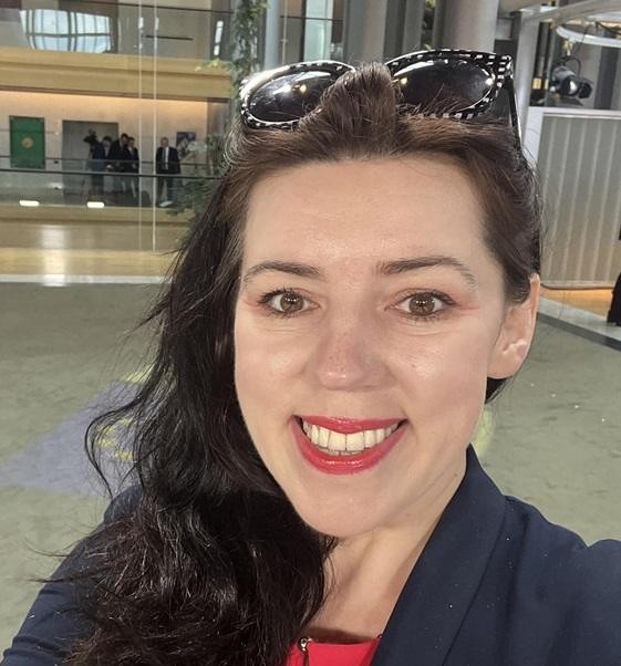 Dominika Ćosić jako korespondentka w Brukseli, aktywnie uczestnicząca w wydarzeniu prasowym, z tłem sugerującym instytucje UE.