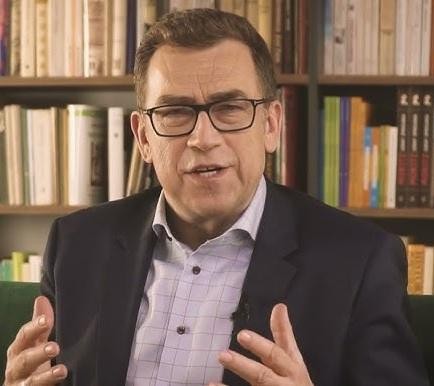 Maciej Orłoś w profesjonalnym ujęciu, uśmiechnięty, na tle nowoczesnego wnętrza, symbolizującego edukację i media.