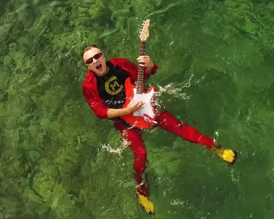 Czadoman w dynamicznej pozie na scenie podczas koncertu, otoczony światłami i roztańczoną publicznością.