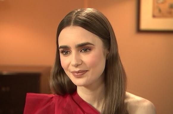 Lily Collins na planie filmowym, w kostiumie, z rozmytym tłem sprzętu produkcyjnego.
