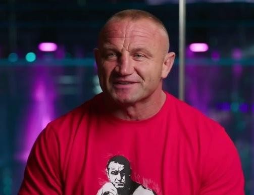Alt: Mariusz Pudzianowski na ringu MMA w dynamicznej pozie bojowej, prezentujący swoją siłę i skupienie podczas walki.