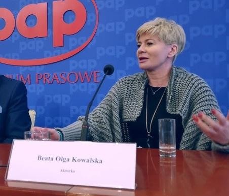 Beata Olga Kowalska na scenie teatralnej podczas występu, w dynamicznej pozie, oddająca emocje roli, z subtelnym tłem scenografii.