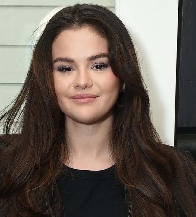 Selena Gomez śpiewająca na scenie, otoczona kolorowymi światłami, z mikrofonem w dłoni.