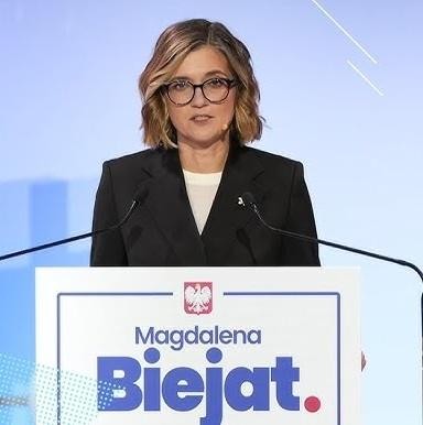 Magdalena Biejat w interakcji z mieszkańcami warszawskiej Pragi, uśmiechnięta i zaangażowana w rozmowę, w tle miejski krajobraz.